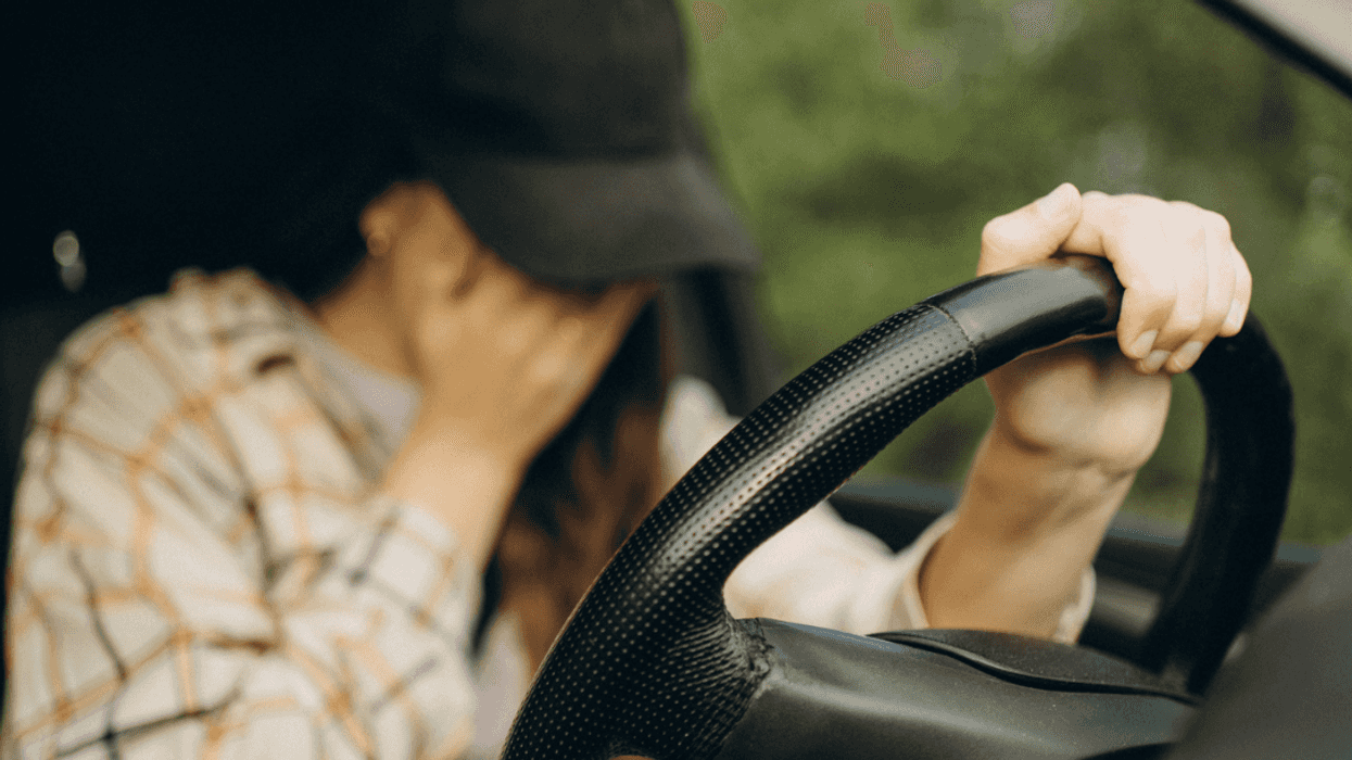 A woman sitting in her car with her head in her hands.