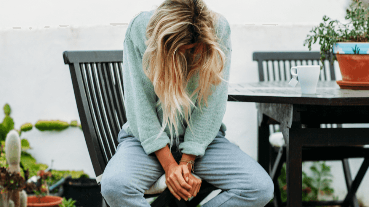 A woman sitting on a deck chair with her head down.