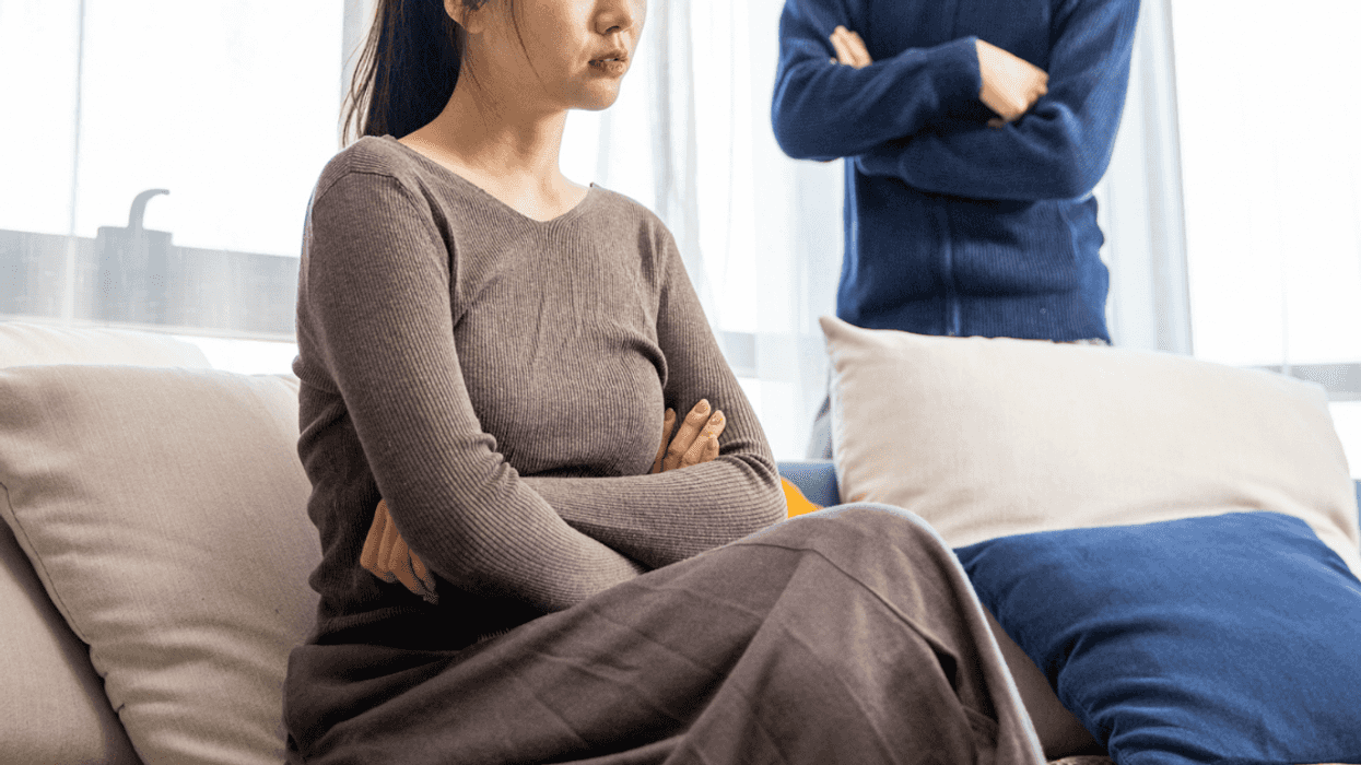 A woman sitting on a sofa with her arms crossed, and a man standing behind her with his arms crossed.