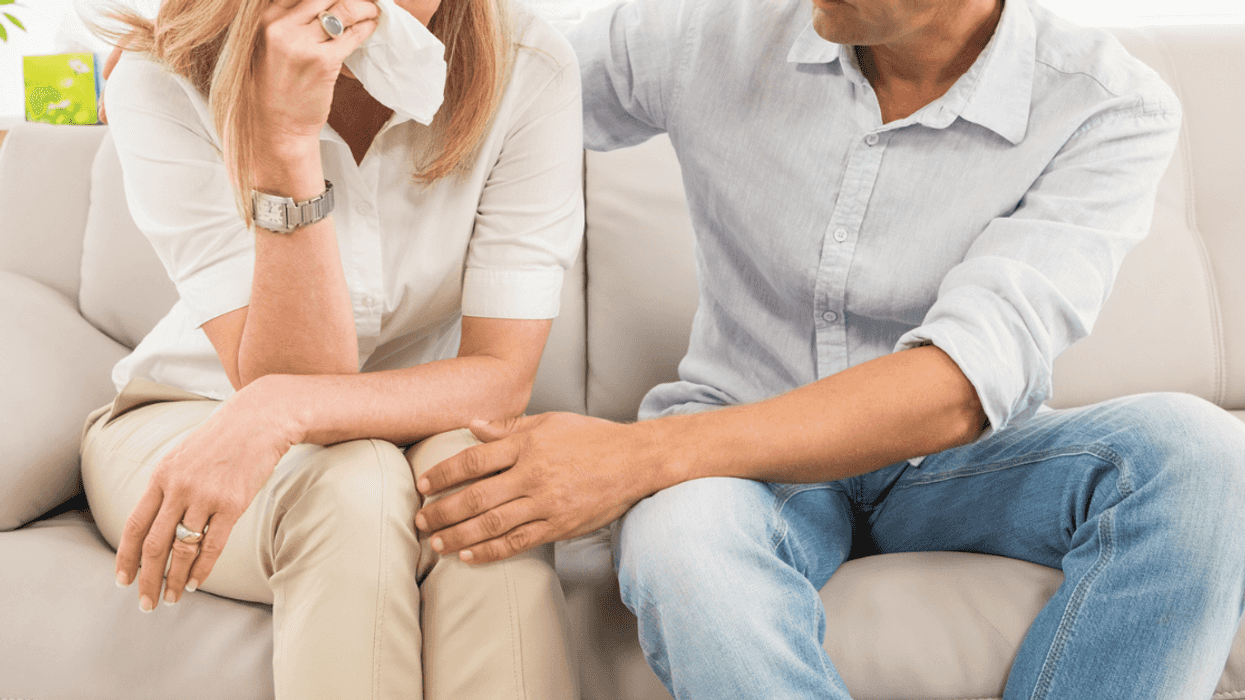 A woman sitting on the sofa crying with a man sitting next to her comforting her.