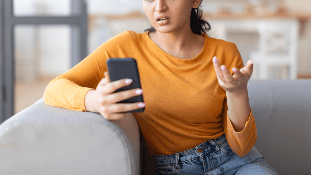 A woman sitting on the sofa, holding her phone, making a gesture with her hand.