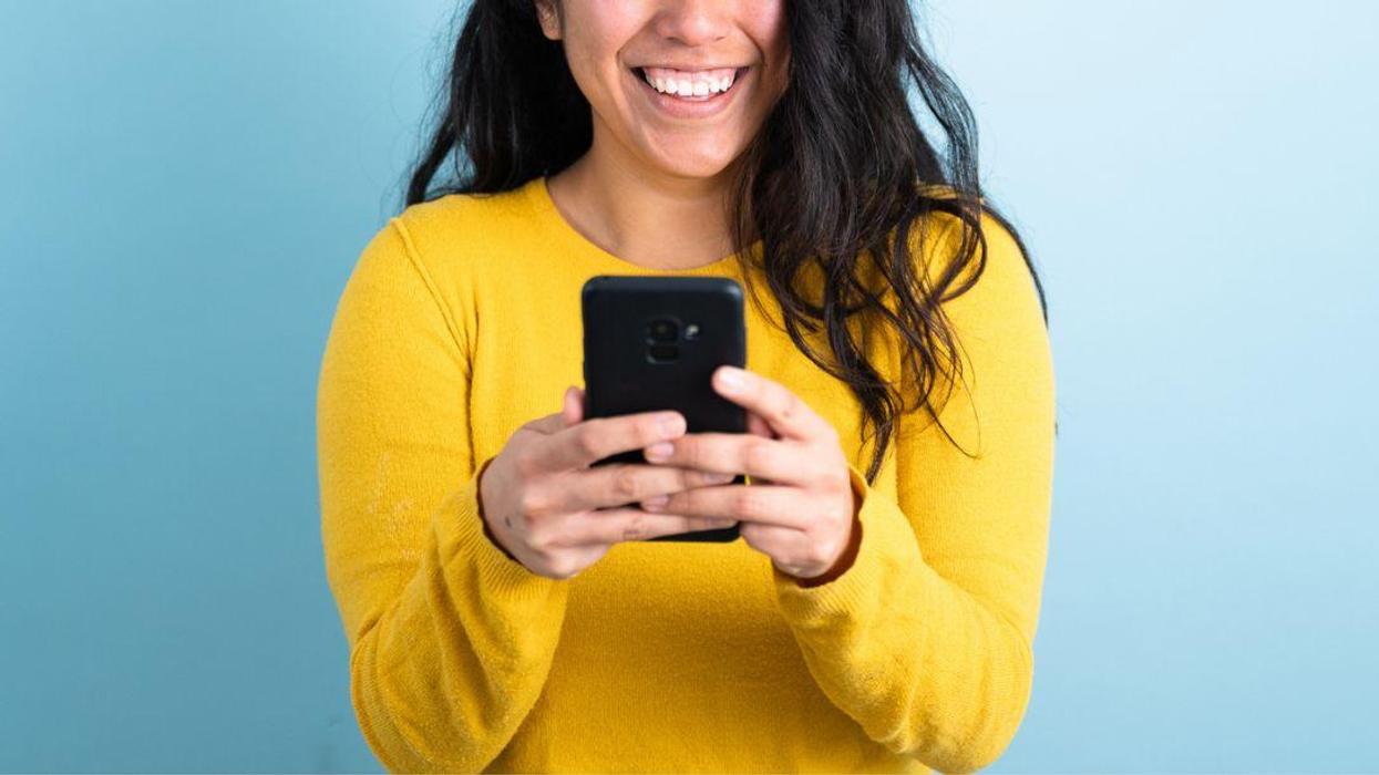 A woman smiling and happy because she has received good news on her phone.