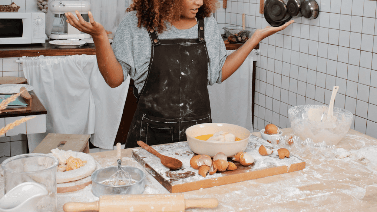A woman standing at a dirty kitchen counter with cracked eggs and a bowl in front of her.