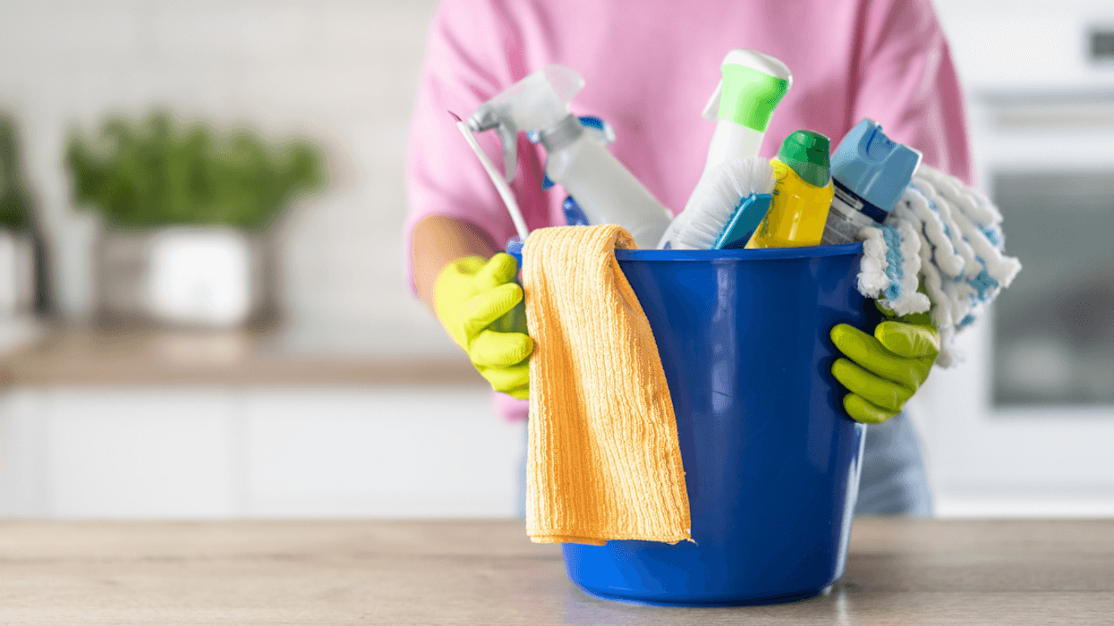 A woman standing behind a bucket of cleaning supplies.