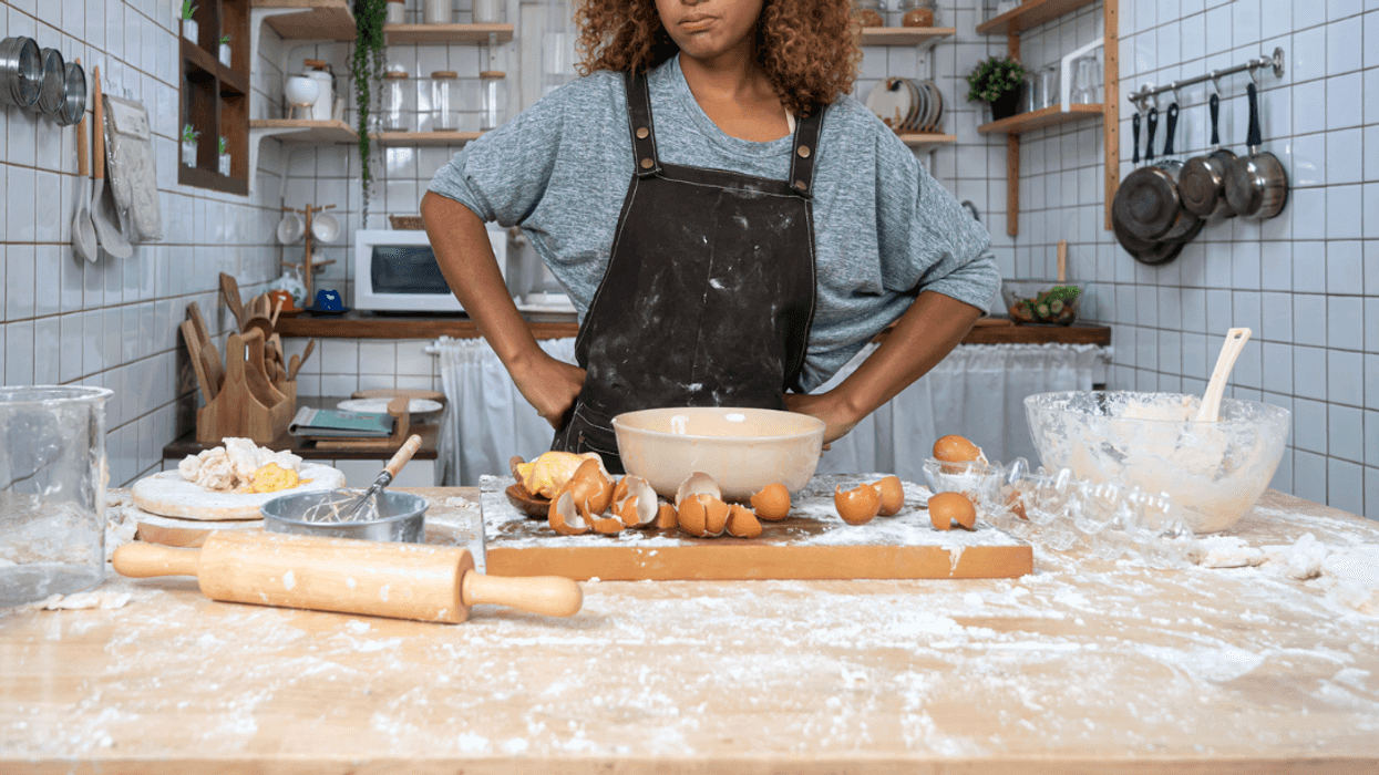 A woman standing behind a messy counter covered in flour and eggshells.