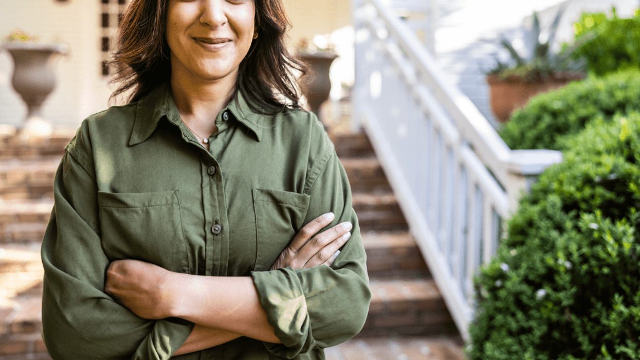A woman standing in front of a house, folding her arms.