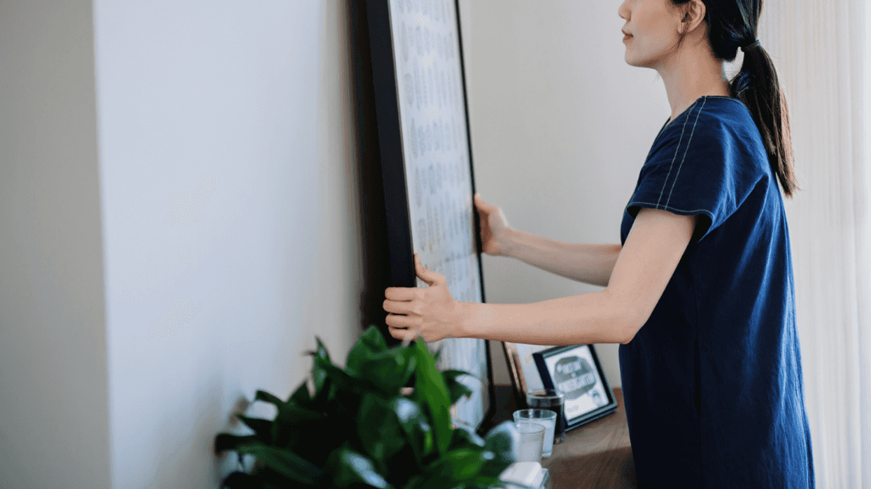 A woman taking down a picture in a frame.