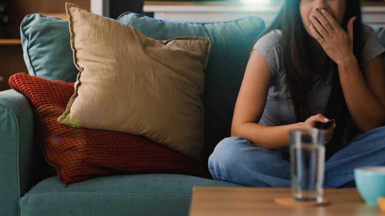 A woman watches a movie on a projector on the couch in her apartment. She seems shocked.