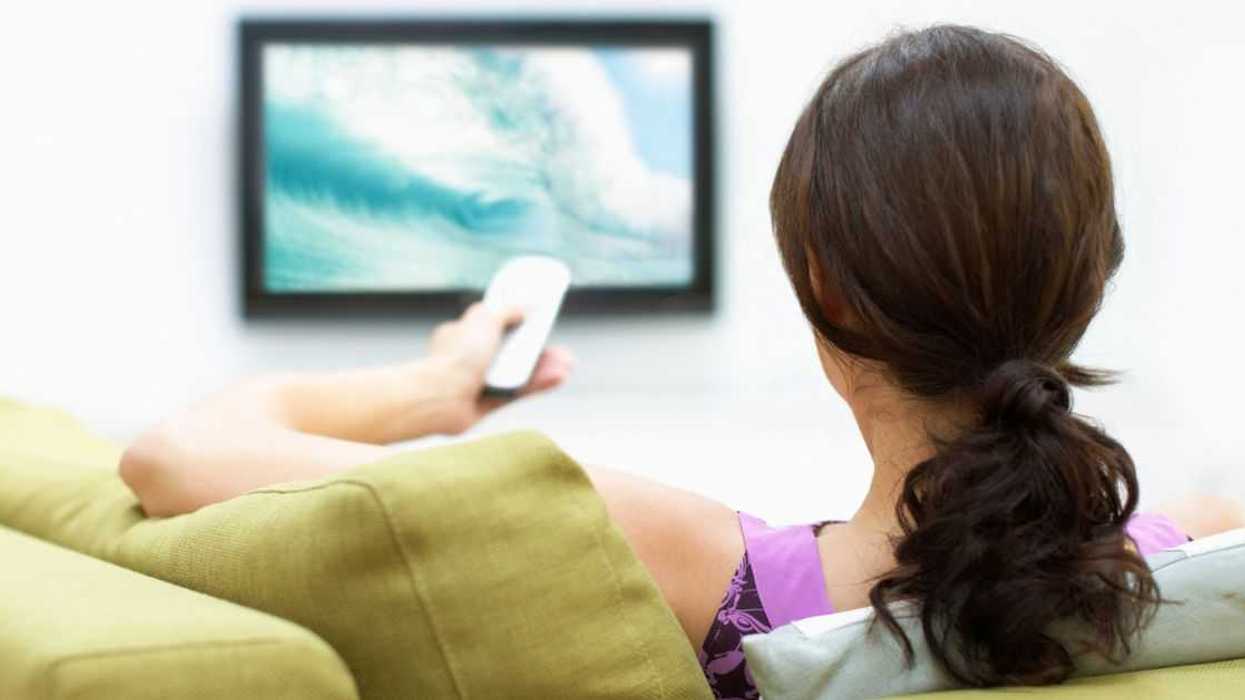 A woman watches TV and uses the remote