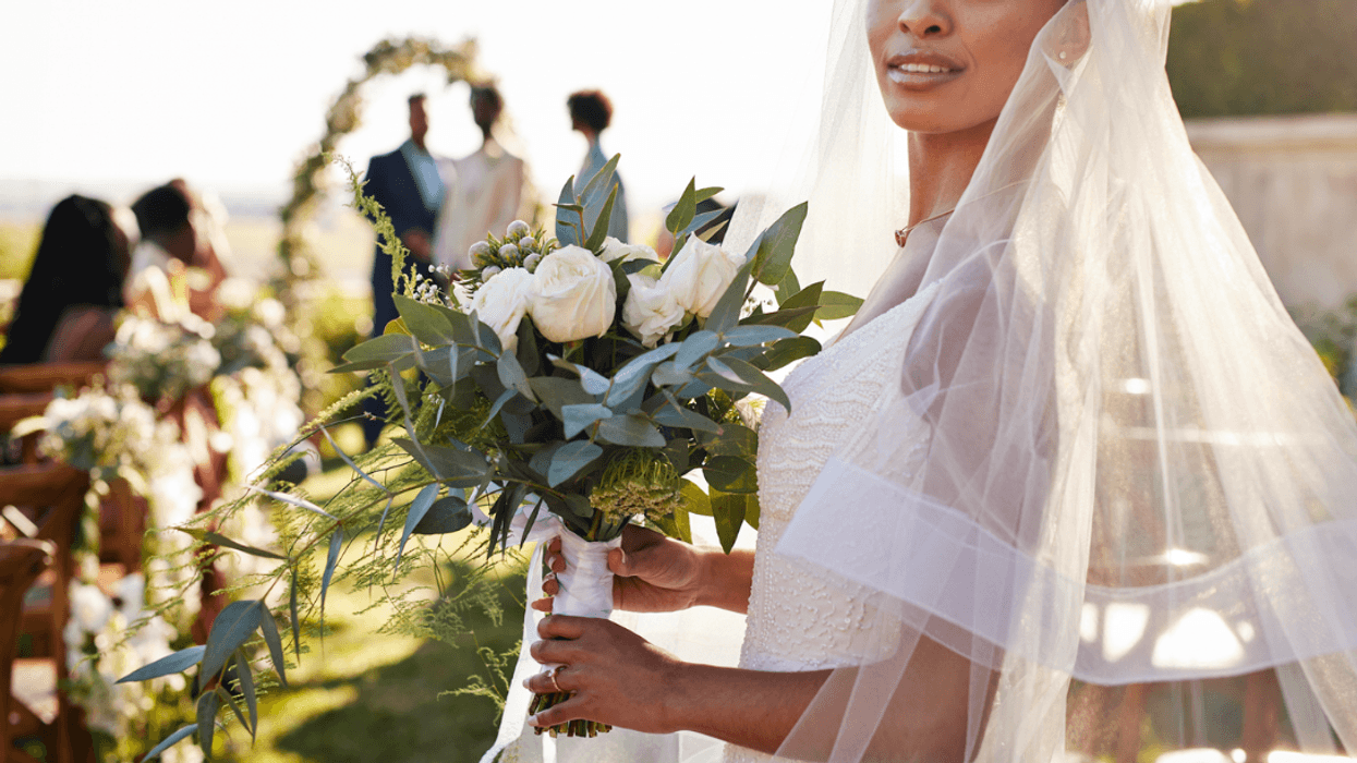 A woman wearing a bridal veil, holding a bouquet standing at the beginning of an aisle.