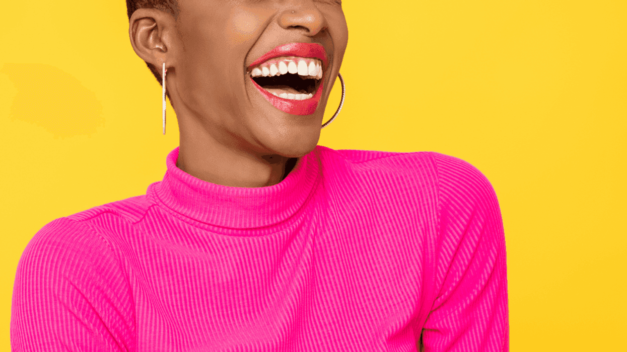 A woman wearing a pink shirt laughing in front of an orange background.