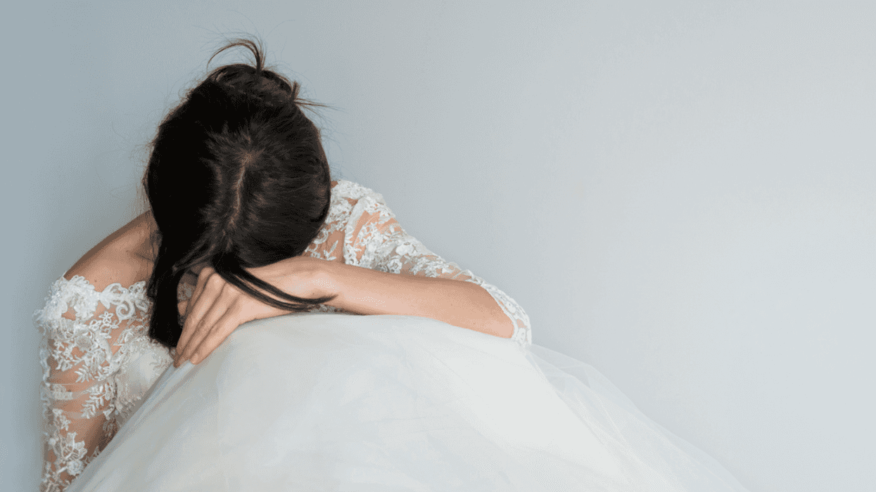 A woman wearing a wedding gown seated with her head in her hands.