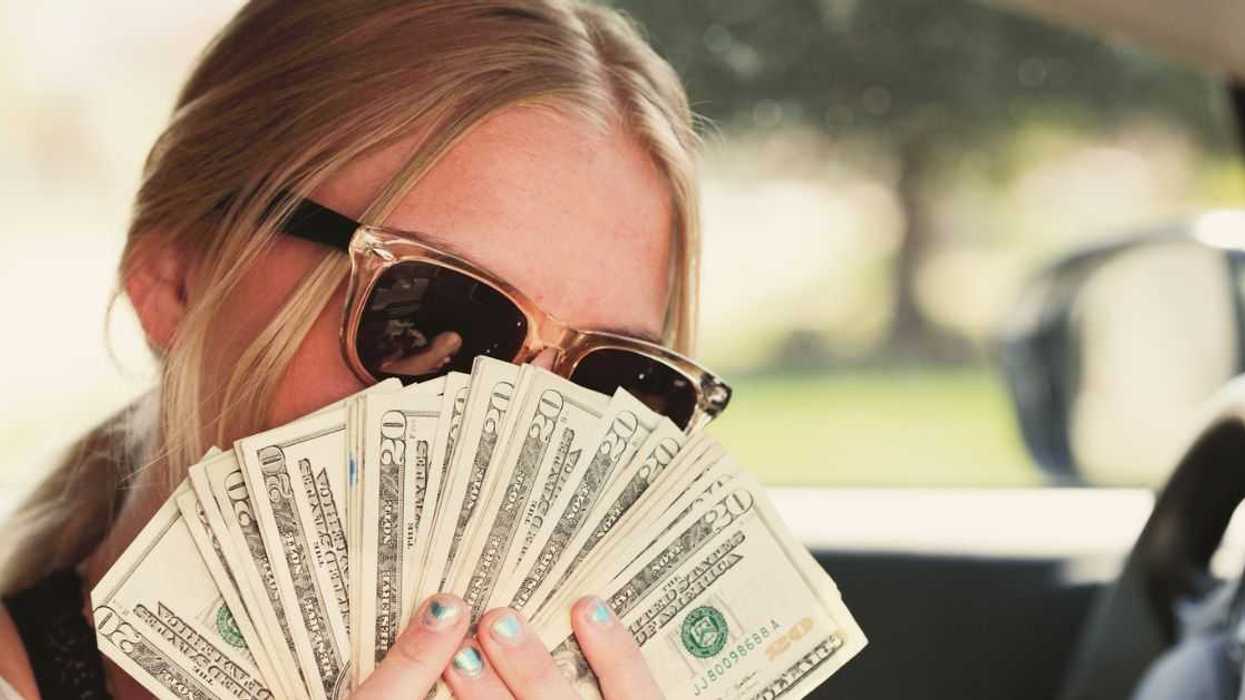 A woman wearing sunglasses holds out a ton of cash