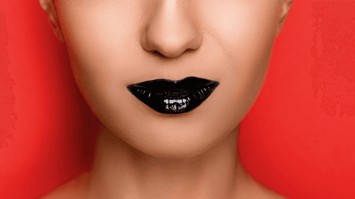 A woman with black lipstick in front of a red background.