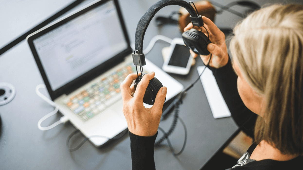 A woman with headphones in her hand looking at a computer.