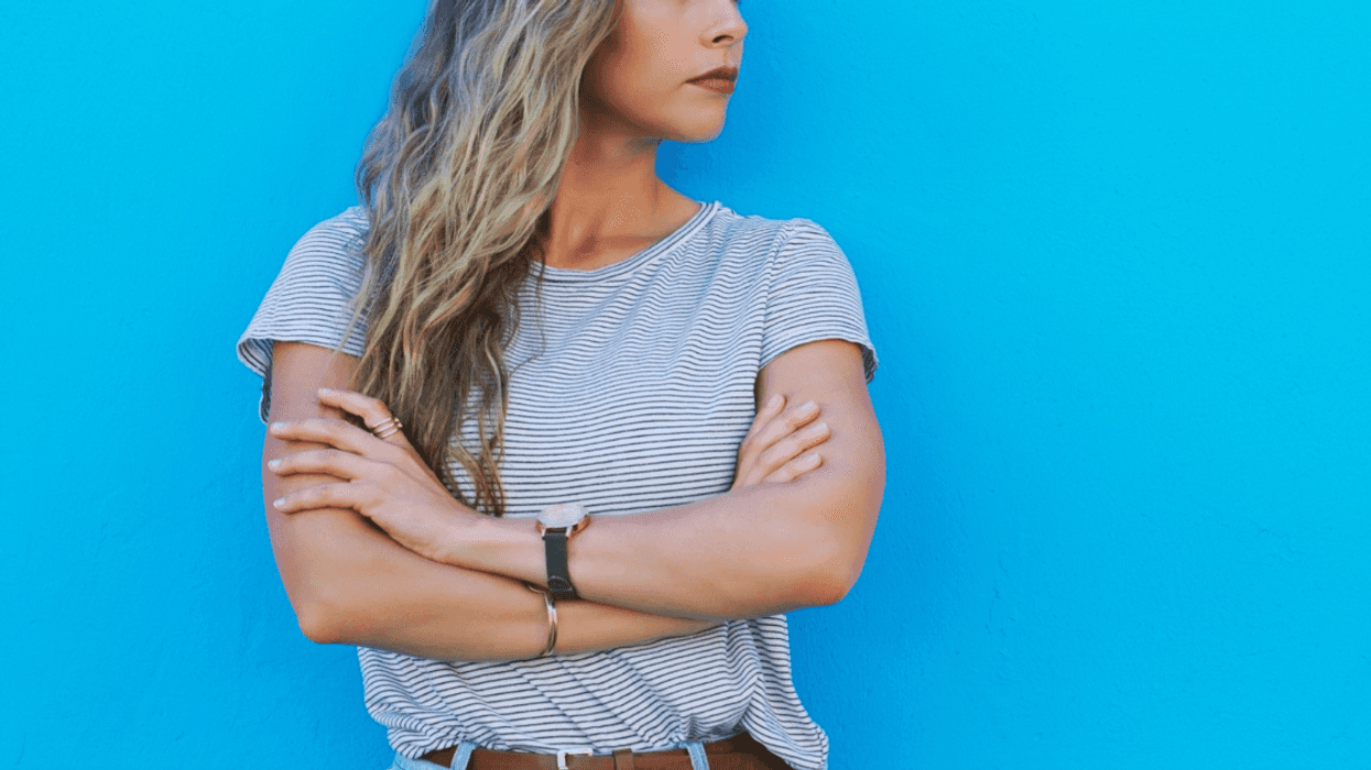 A woman with her arms crossed against a blue background.