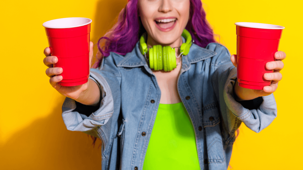 A woman with purple hair holding two red plastic cups.