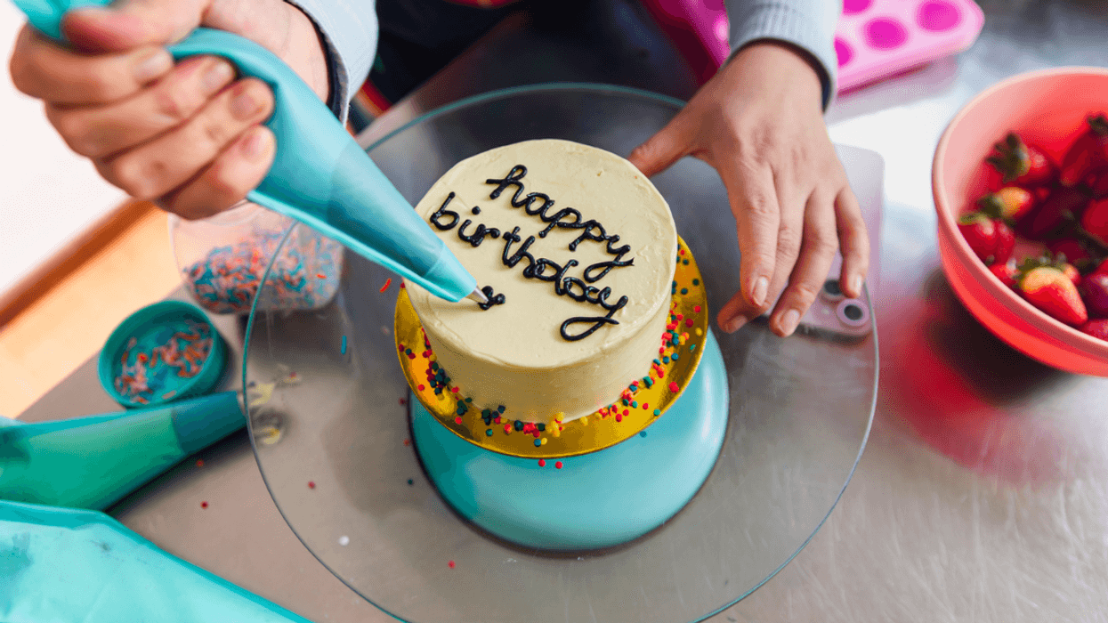 A woman writing happy birthday on a cake with a pastry bag.