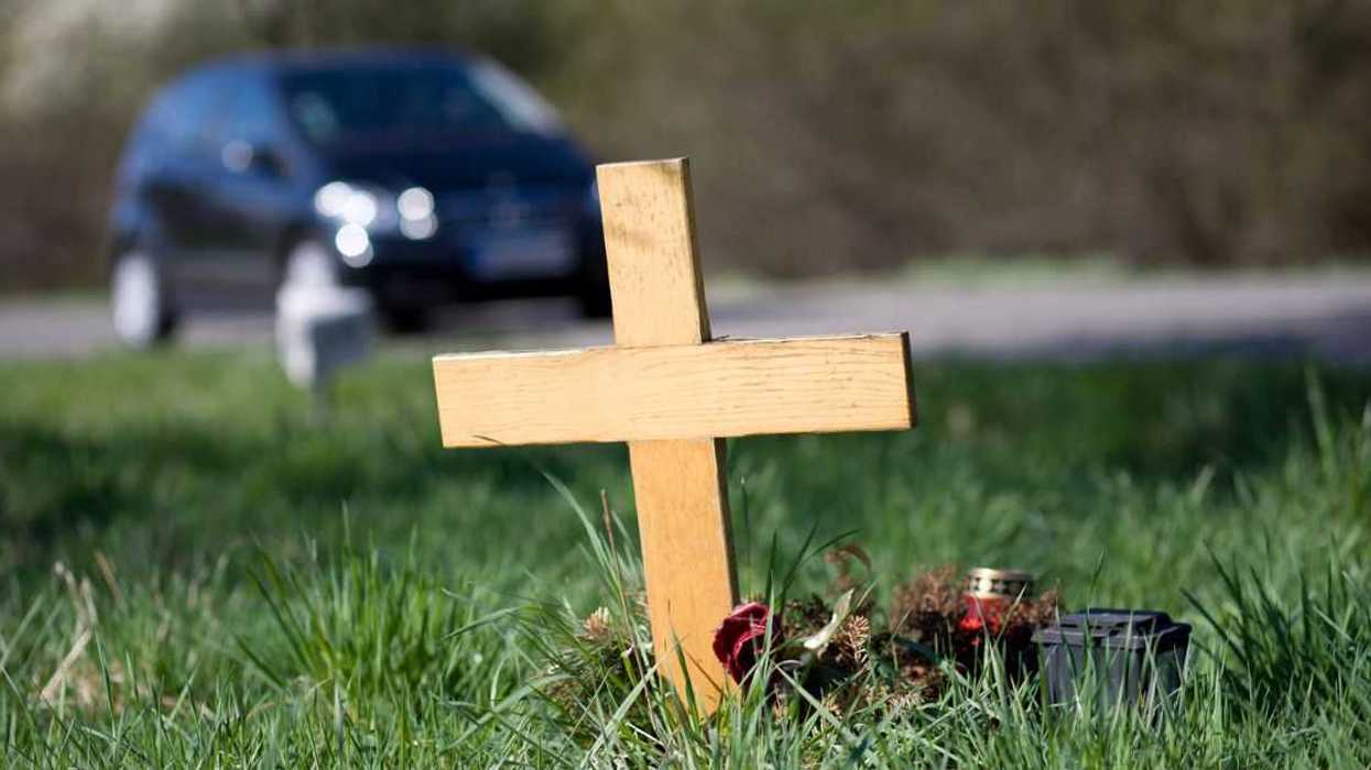 A wooden roadside memorial. In the background an unrecognisable car drives by the scenery.