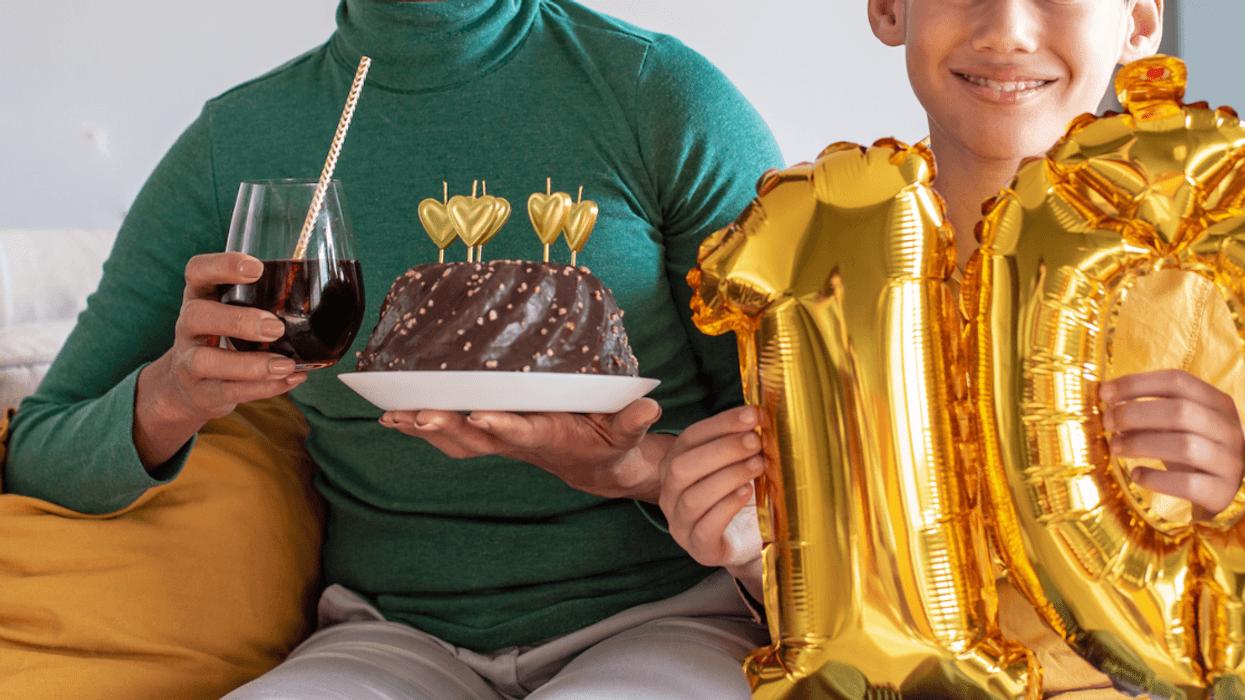A you holding golden number 10 balloons sitting next to a woman holding a cake and a drink.
