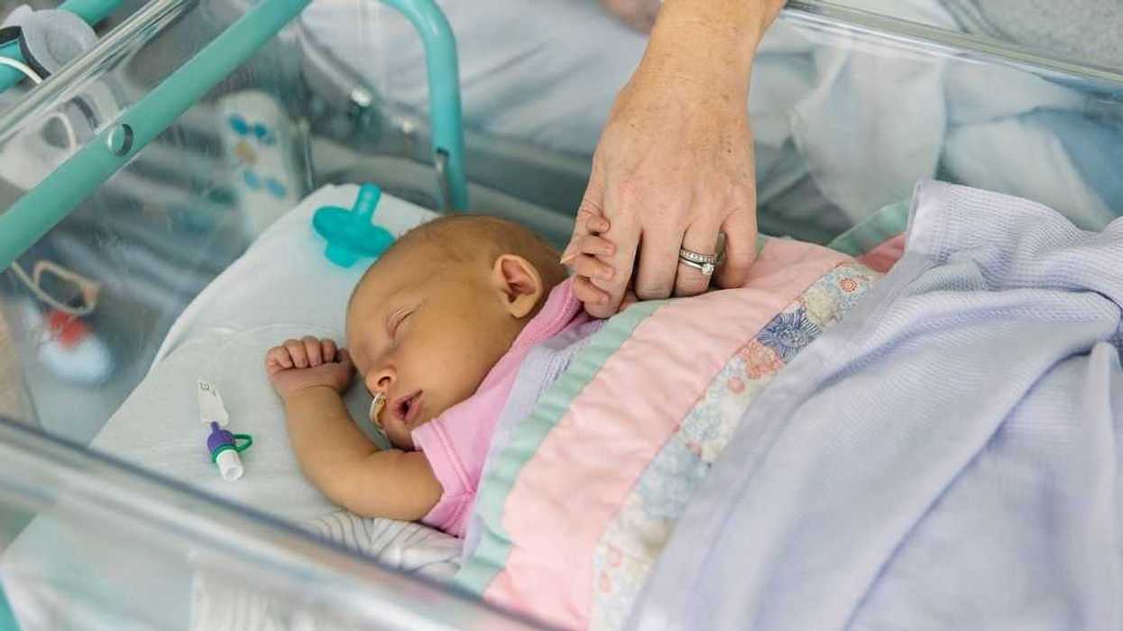 A young baby girl lies in a hospital cot. She is suffering from neonatal jaundice. Her mother holds her hand and comforts her as she sleeps.
