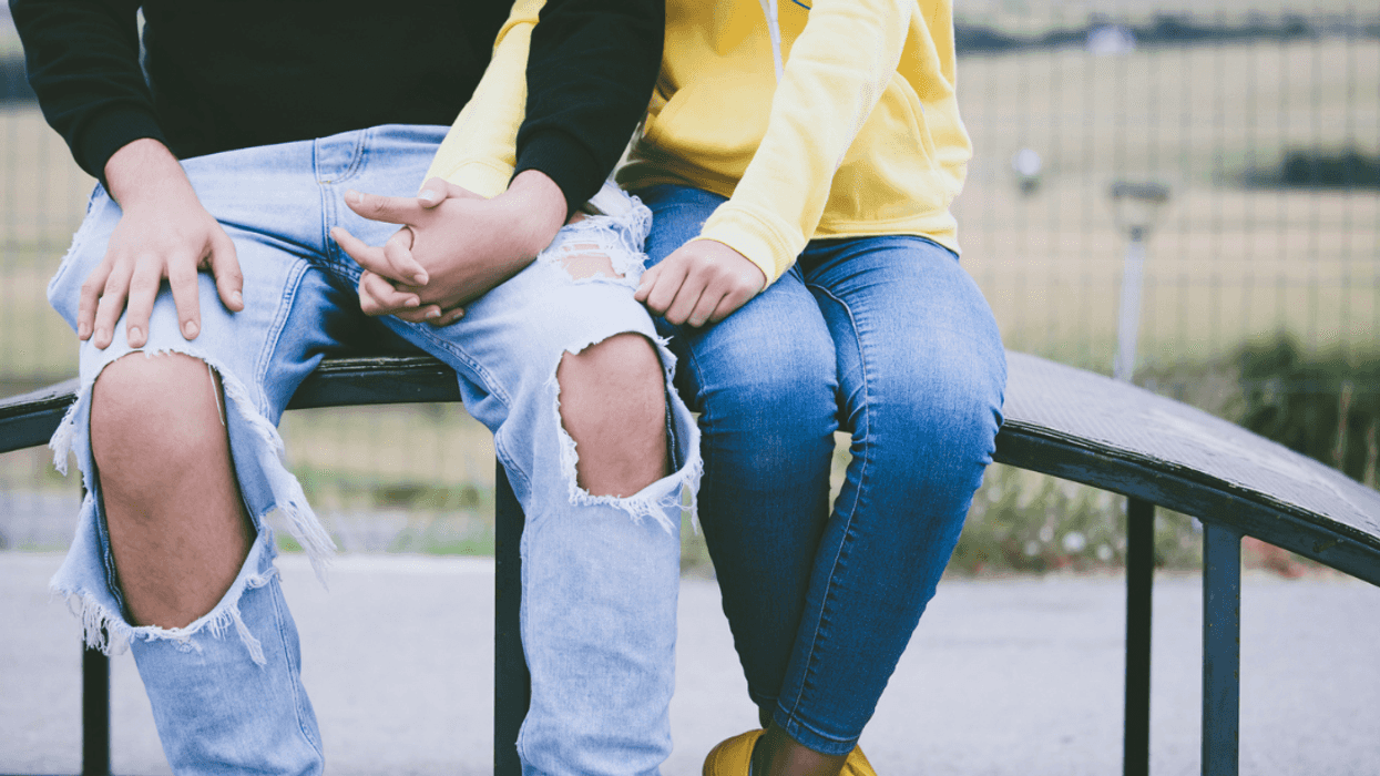 A young boy and a young girl holding hands, sitting on a rail.