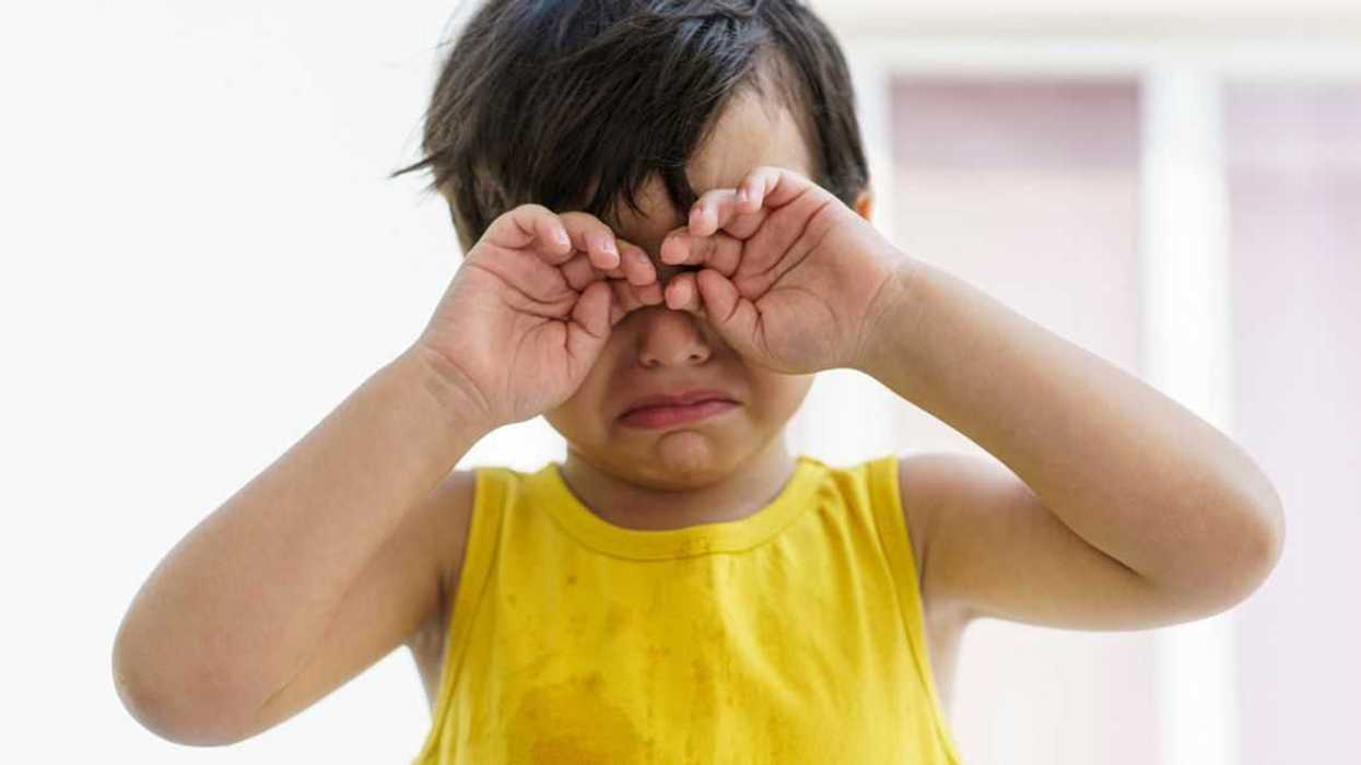 A young boy cries and rubs his eyes