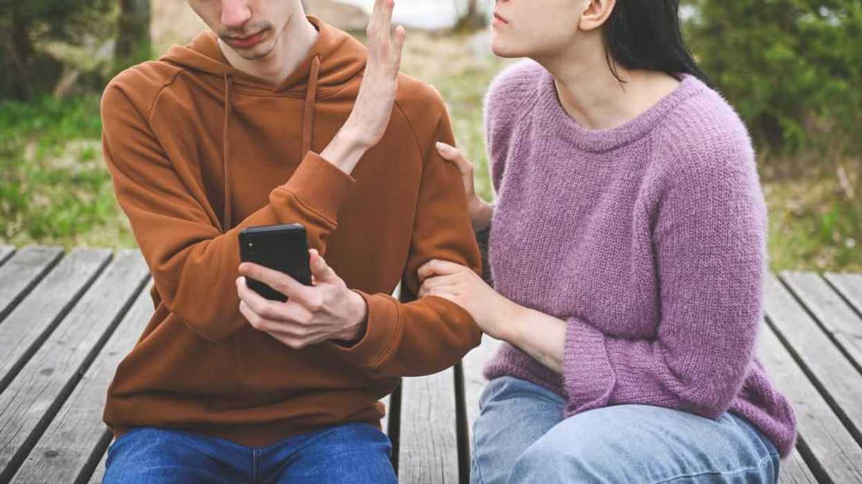 A young couple sit on a boardwalk midday, while in the middle of a quarrel.