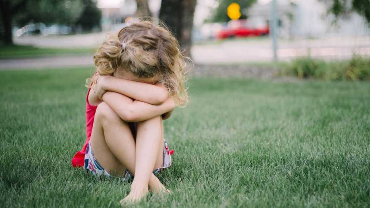 A young girl sits in the grass with her face collapsed into her arms