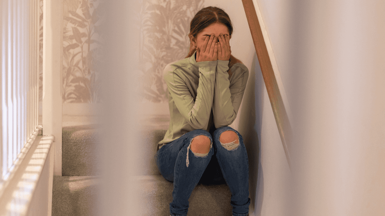 A young girl sitting on the stairs with her head in her hands.