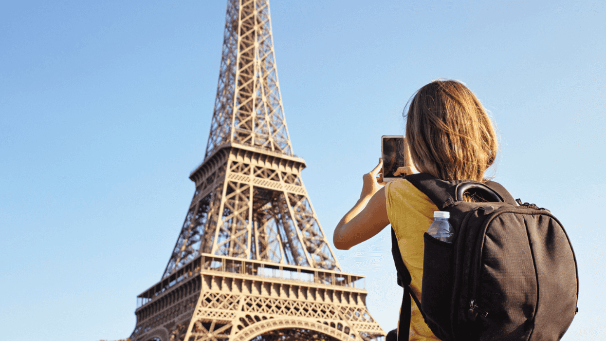 A young girl taking a picture of the Eiffel Tower with her phone.