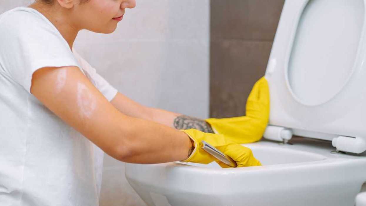 A young girl wearing yellow household gloves cleans the toilet bowl. House cleanliness, cleaning service.