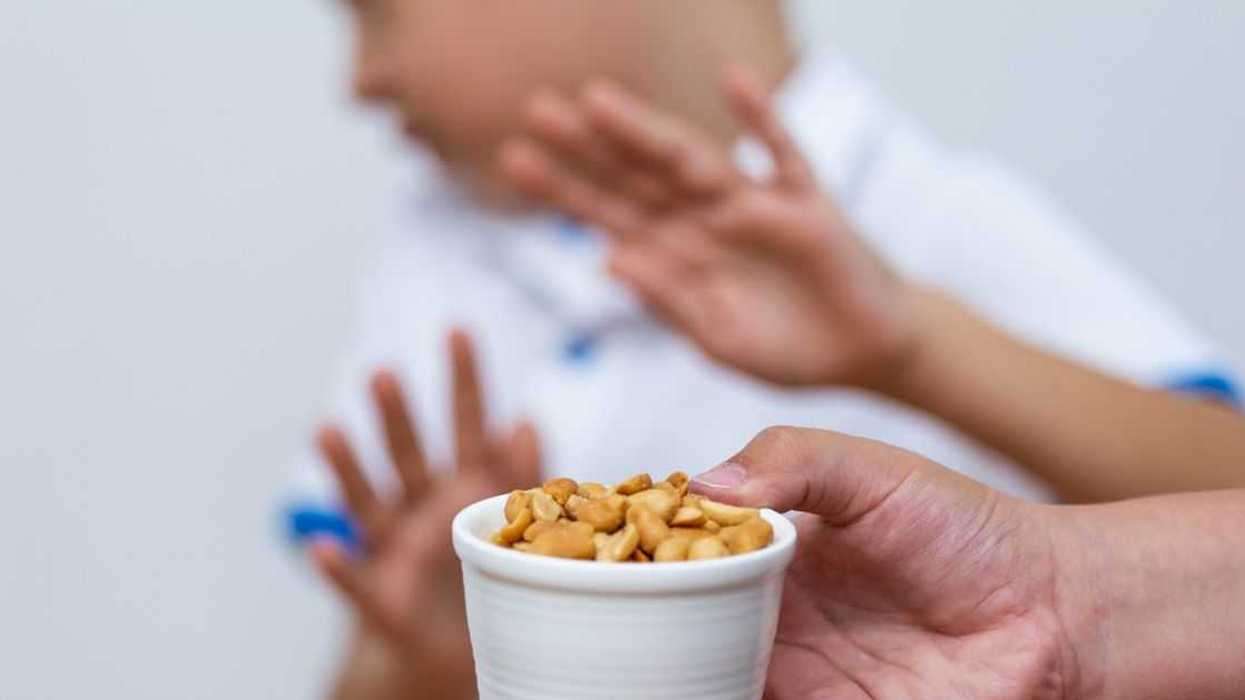 A young man pushes away a bowl of peanuts offered by an adult.
