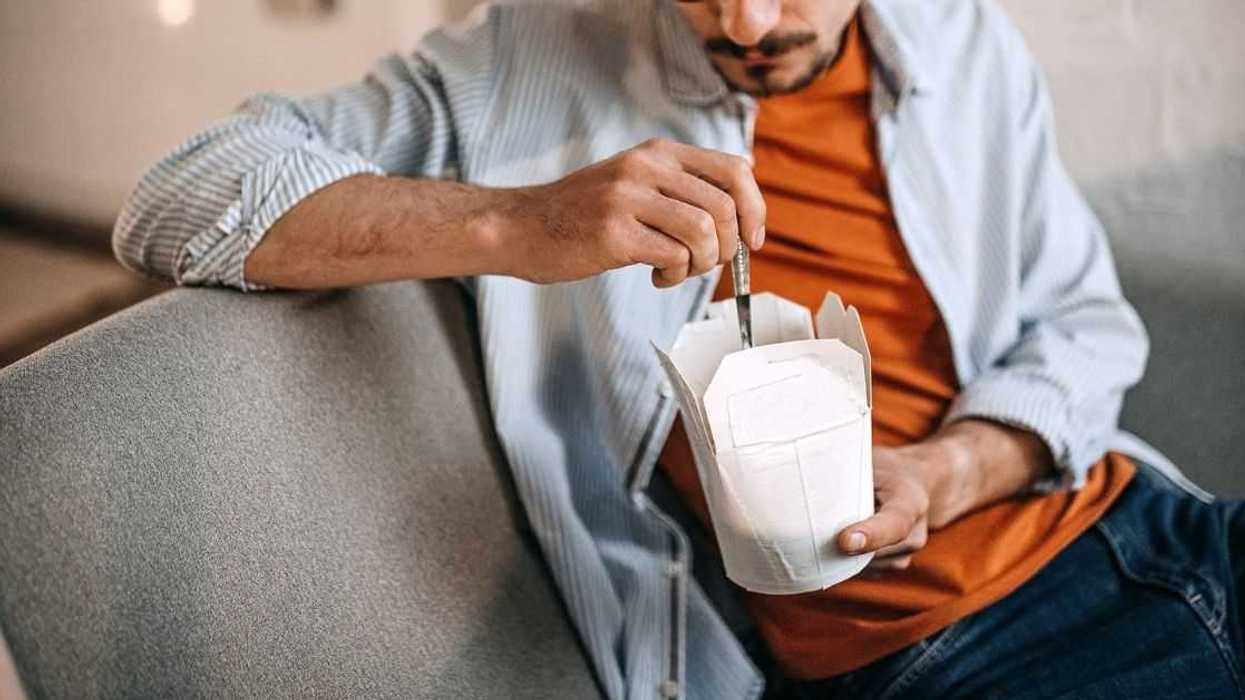 A young man with glasses sits on a couch eating out of a carton.
