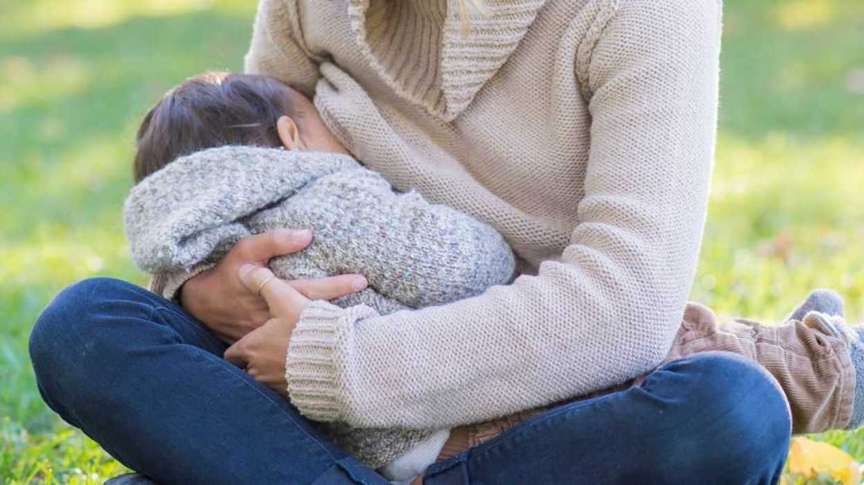 A young mother of mixed breastfeeds her baby boy in a public park. She looks down at him while he feeds.
