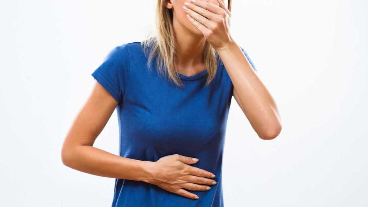 A young sick woman covers her mouth and holds her stomach.