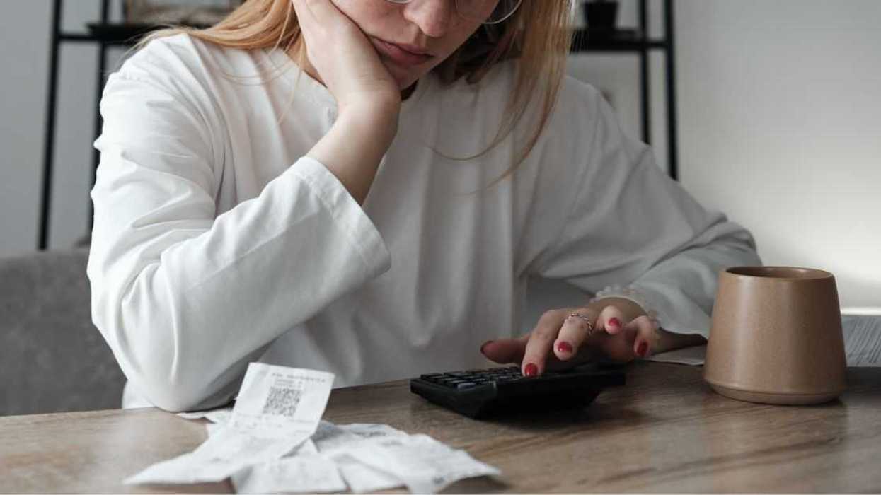A young woman calculating spendings while looking at bills . She is using a calculator while sitting at the table.