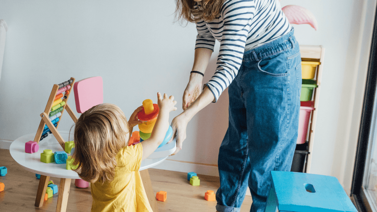 A young woman handing a toddler a toy.