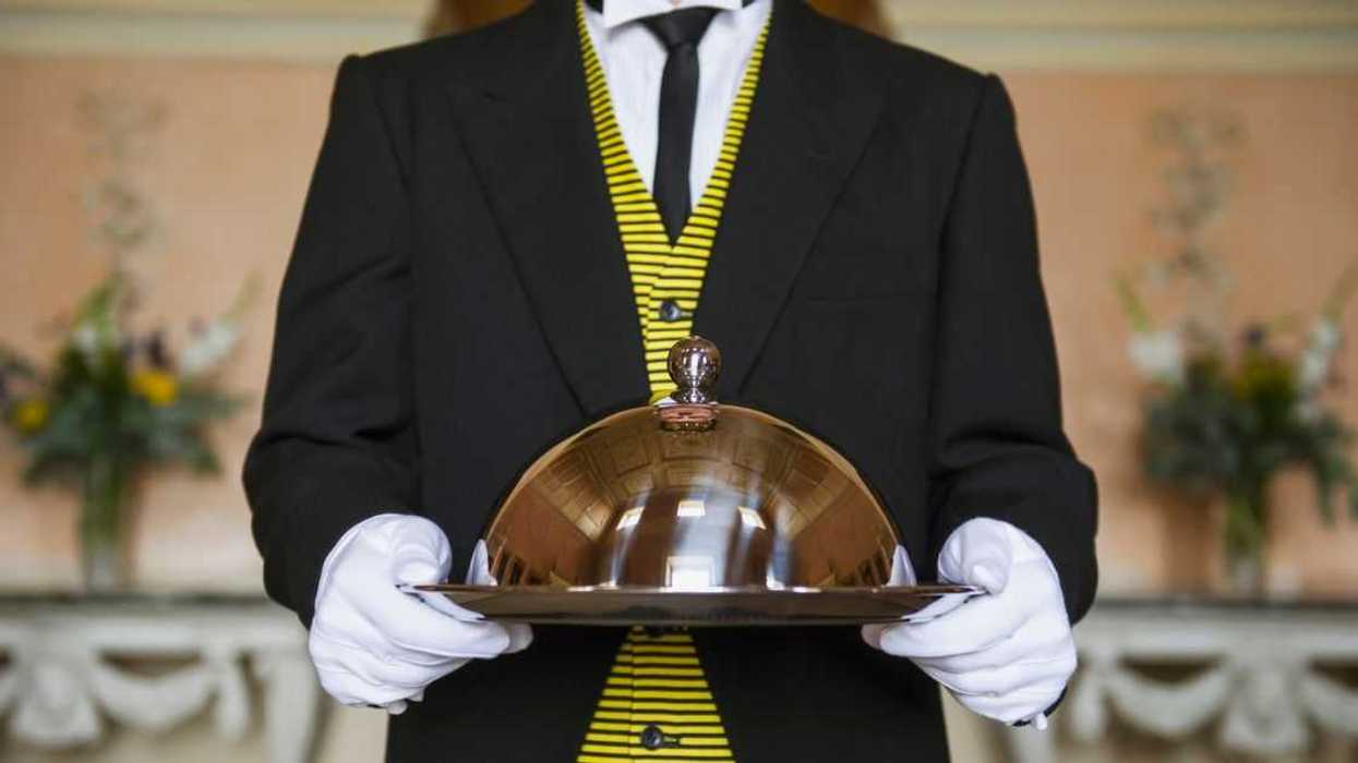 Adult male butler holding serving tray in formal parlor.