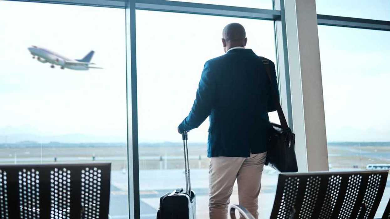 Airport, suitcase and businessman waiting to board flight by the terminal for corporate work trip. Travel, luggage and professional male traveler watching flying plane by a window in terminus lounge.