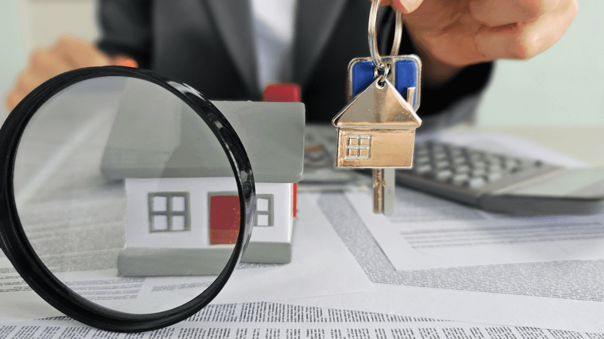 Aman holding a key above paperwork with a magnifying glass in front.