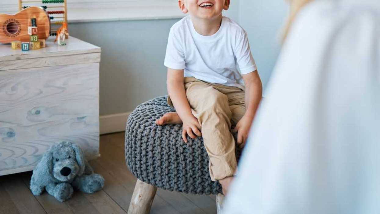 An adorable little boy sitting on a chair while talking to a therapist.