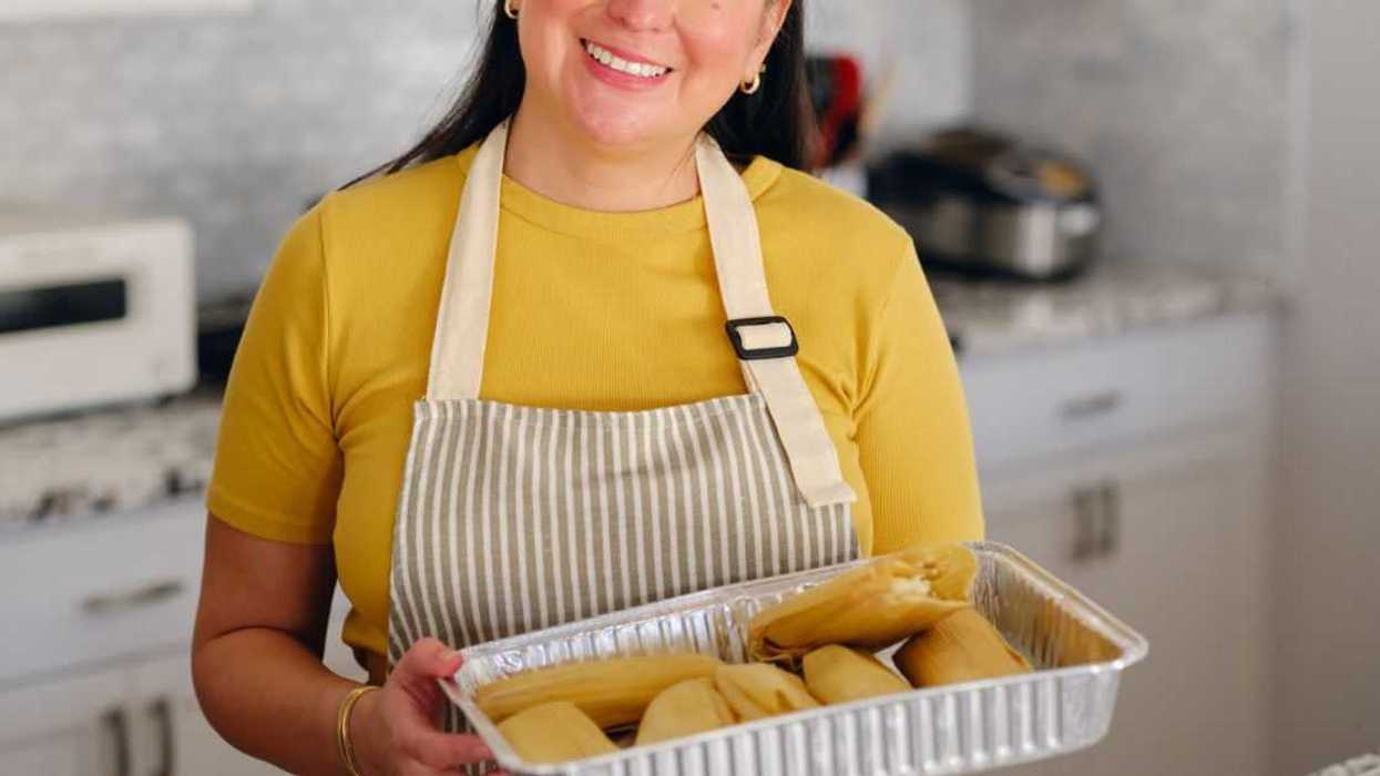 An adult woman making tamales and serving her family in a home kitchen.