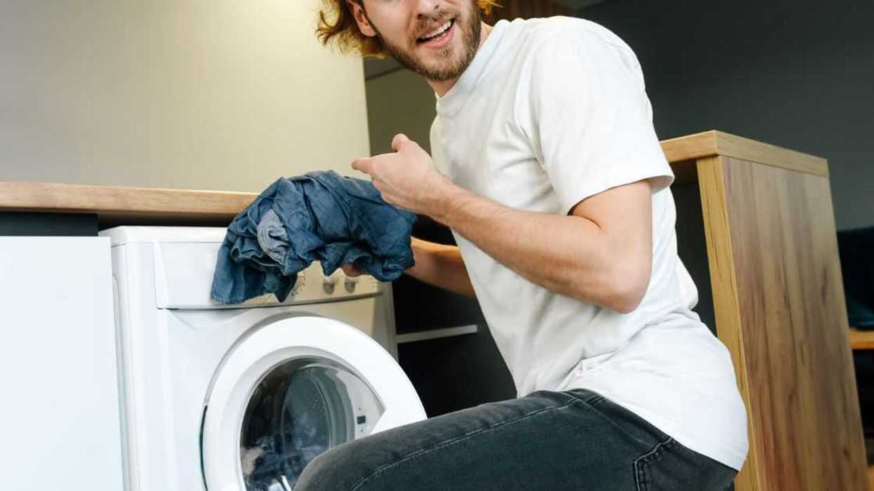 An angry young man is throwing things into the washing machine. Domestic quarrel.