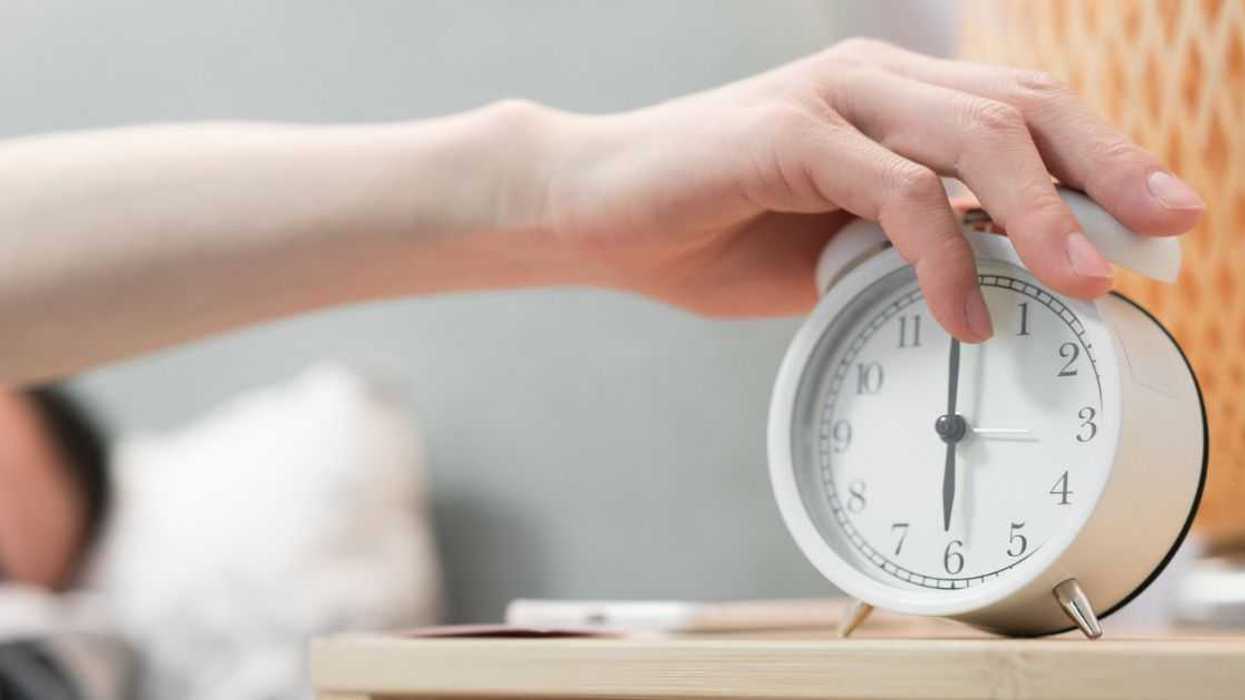 An asleep man is turning off alarm clock.