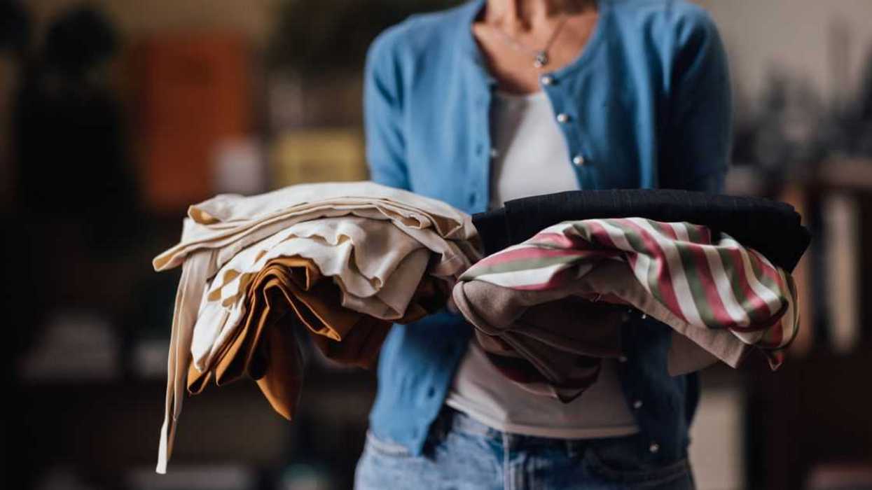 An elderly woman carries a stack of neatly folded clothes.