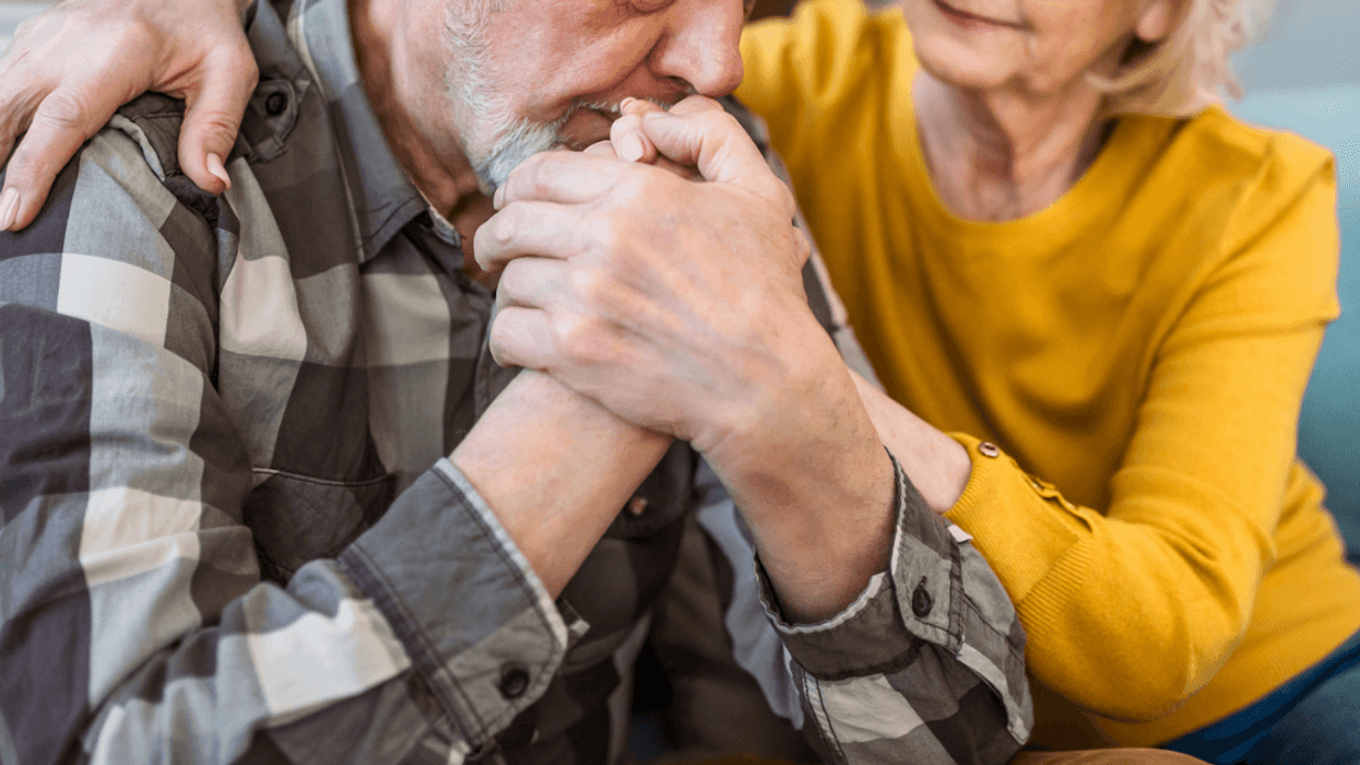 An older man resting his head on his hands and a woman leaning in to comfort him.