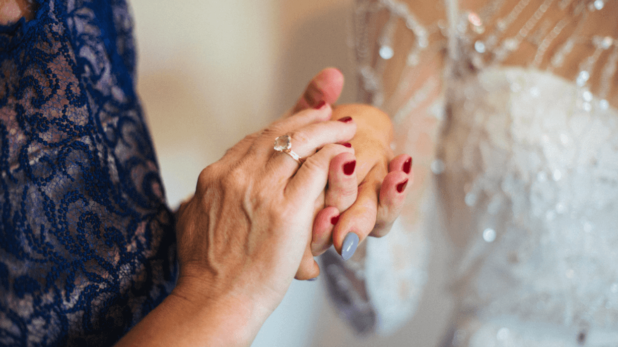 An older woman in an evening gown holding the hand of a bride.