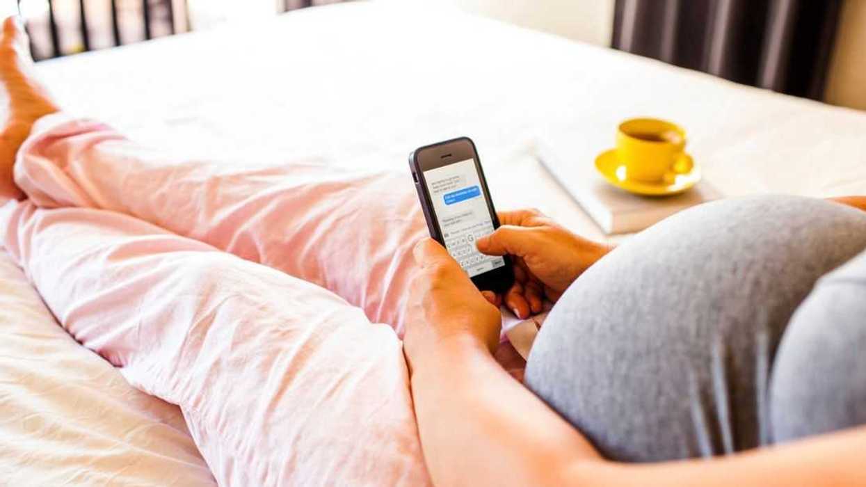 An unrecognizable pregnant Caucasian woman using cell phone in bed.