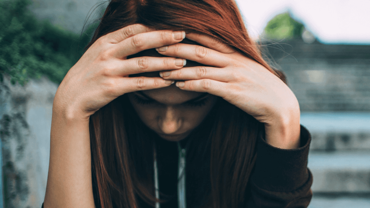 an upset teen girl sits on steps with her head in her hands